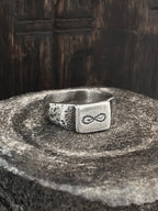 A handmade sterling silver ring with a hand-drawn infinity snake etched on the face