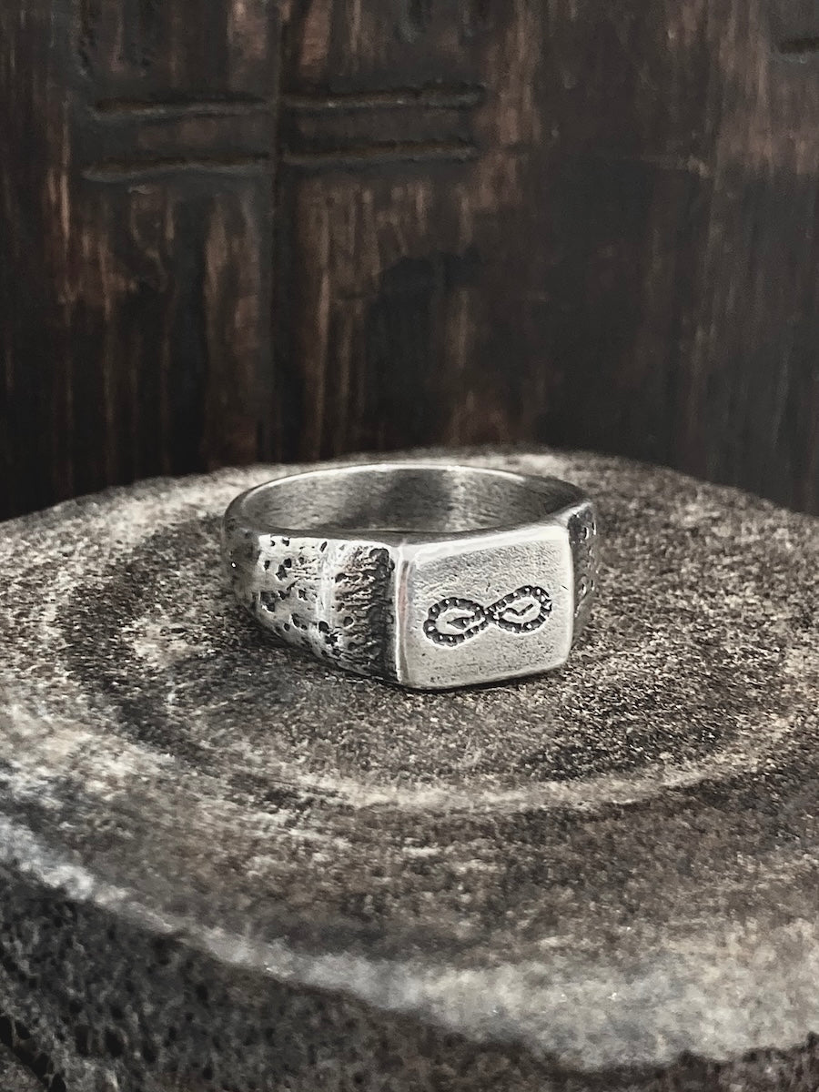 A handmade sterling silver ring with a hand-drawn infinity snake etched on the face