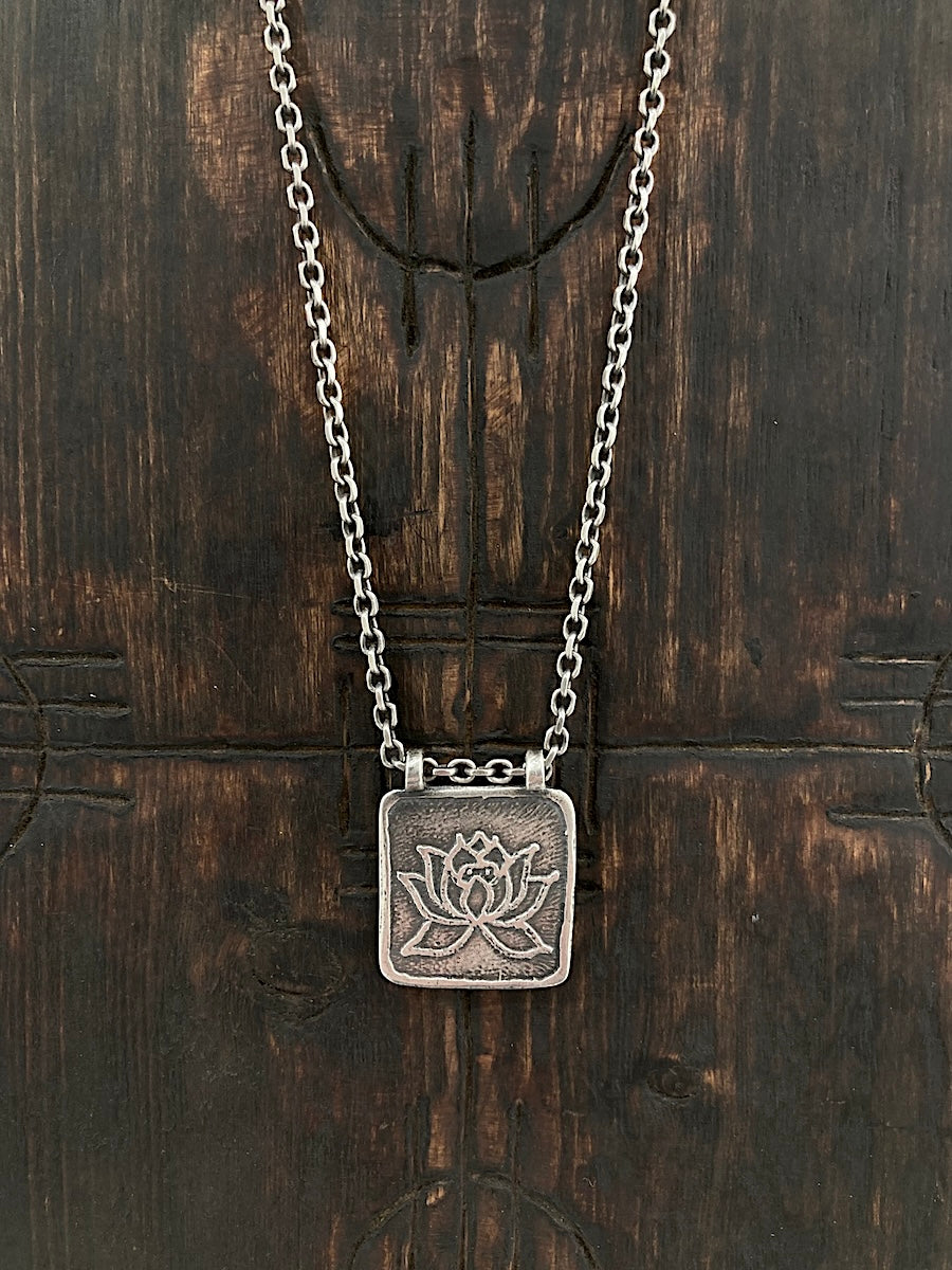 An aged 925 sterling silver Lotus Flower necklace. The lotus represents beauty and purity. Our Lotus pendant has an organic border and wood block effect.