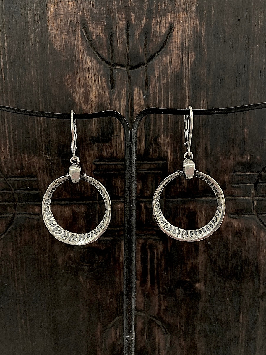 A pair of sterling silver hoop earrings with a flame pattern etched inside representing an eclipse