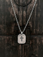 A sterling silver necklace with a rectangular pendant featuring a carved cross.