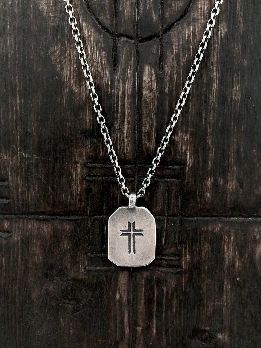A sterling silver necklace with a rectangular pendant featuring a carved cross.