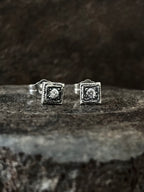 A pair of silver handmade stud earrings with beaded design and centered with a diamond.