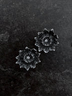 A pair of sterling silver earrings with black oxidized details and centered with diamonds, cast from a poppy pod.