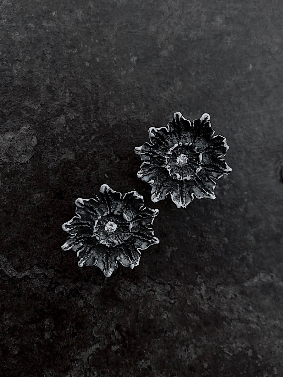 A pair of sterling silver earrings with black oxidized details and centered with diamonds, cast from a poppy pod.